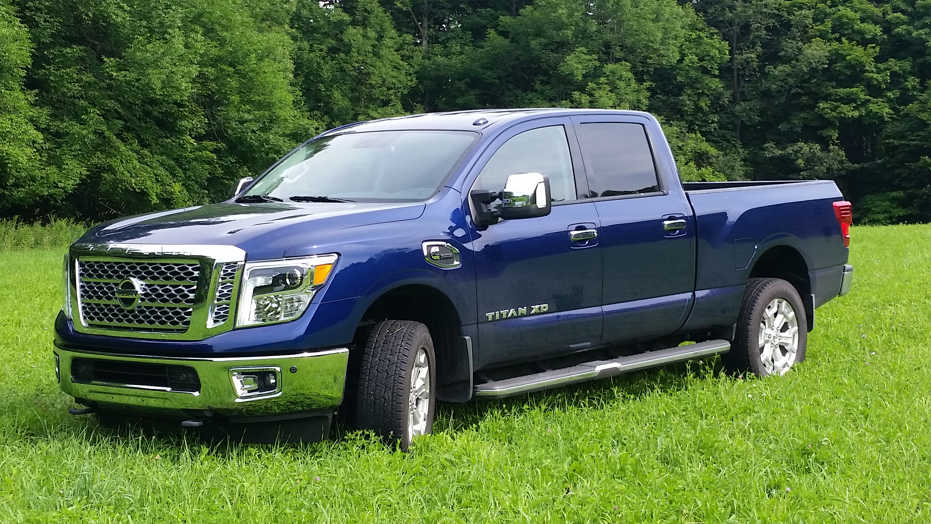 The 2016 Nissan Titan XD SL 4WD CC in Deep Blue Pearl w/ running board lights and splash guards out in the fields of New York State.