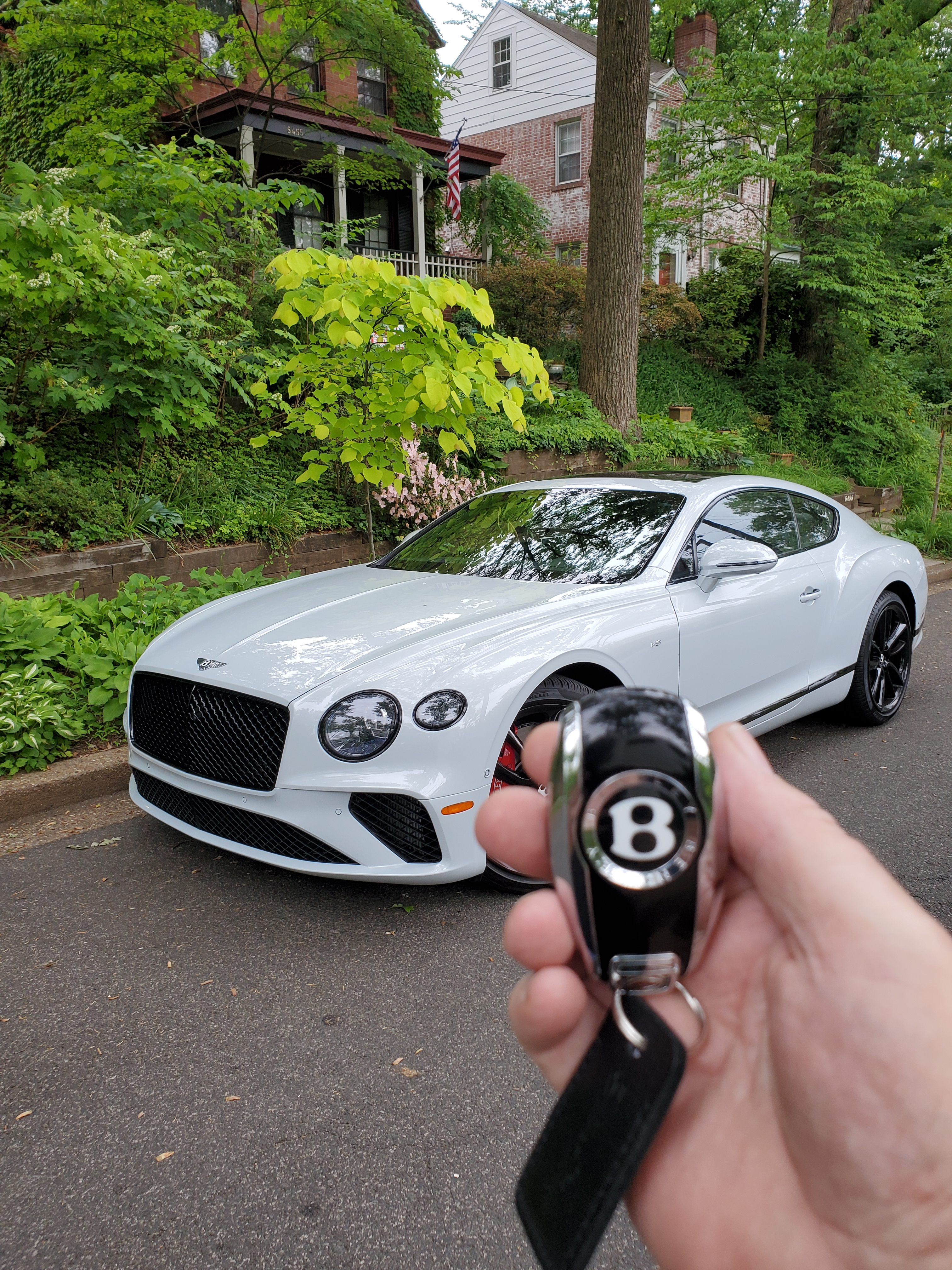 bentley continental gt v8 with key being held in front of it with a green space and house behind it
