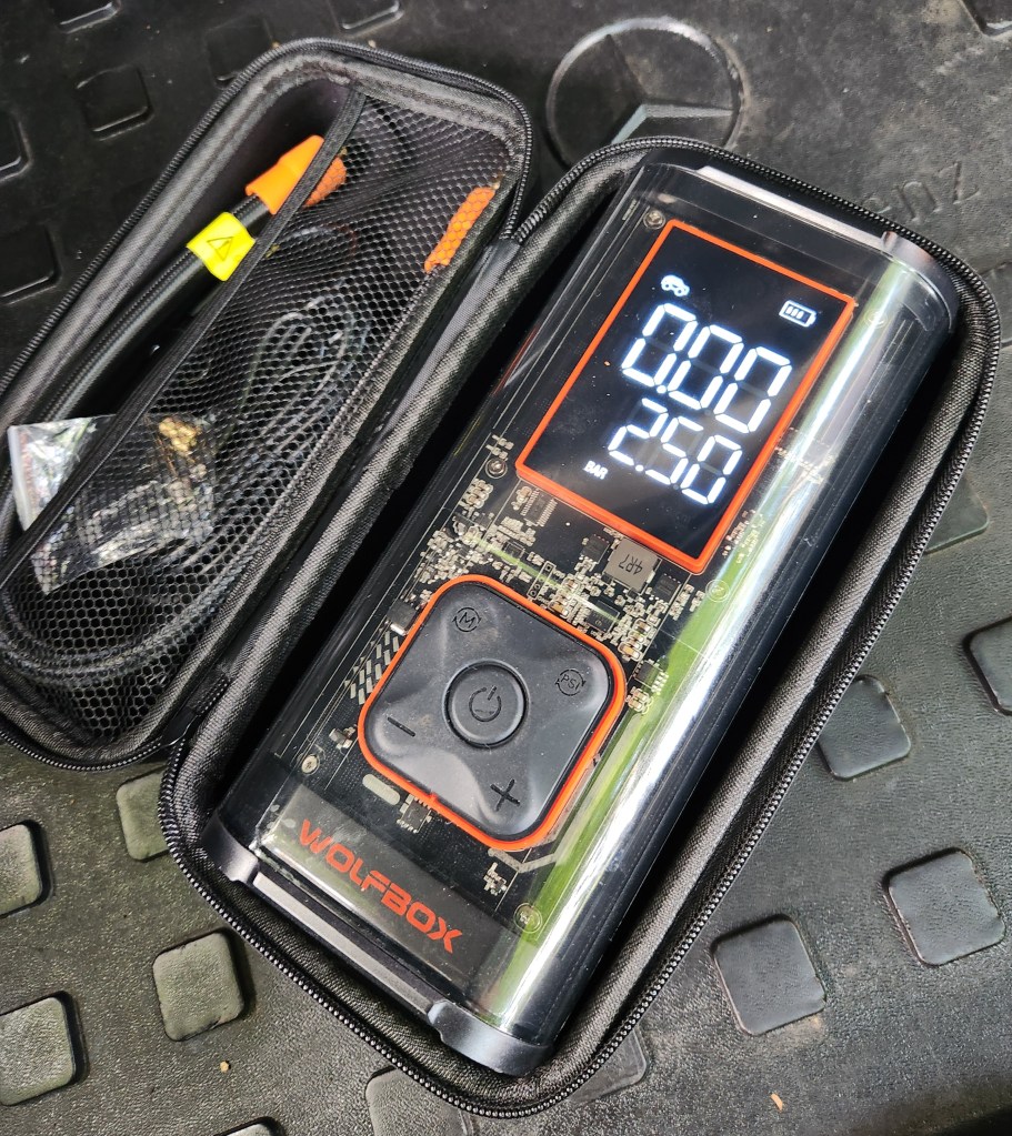 The hard case open with the Wolfbox MegaFlow 24 Pro Portable Tire Inflator, its hose and power cords.